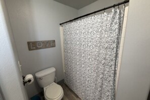 A bathroom with a toilet, a shower curtain, and a wall-mounted sign that says 'LOVE'.