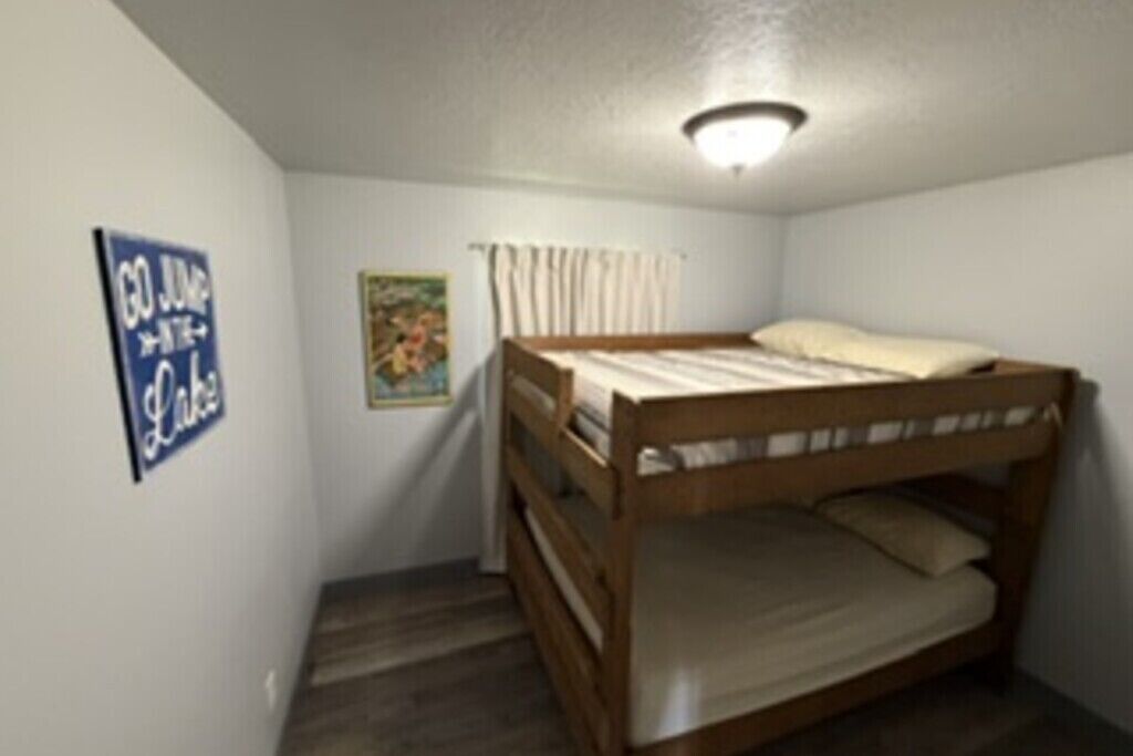 A small, single-bedded room with a bunk bed, a ceiling light fixture, a poster on the wall, and a window with curtains.