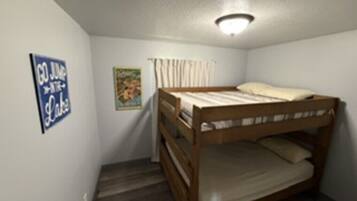 A small, single-bedded room with a bunk bed, a ceiling light fixture, a poster on the wall, and a window with curtains.