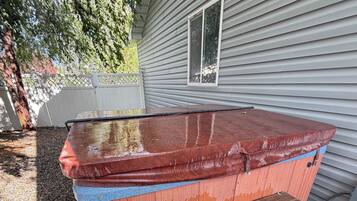 A hot tub with a wooden deck and steps, adjacent to a house with siding and a window.