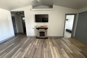 A room with a fireplace, a flat-screen TV mounted above it, and a wooden floor.