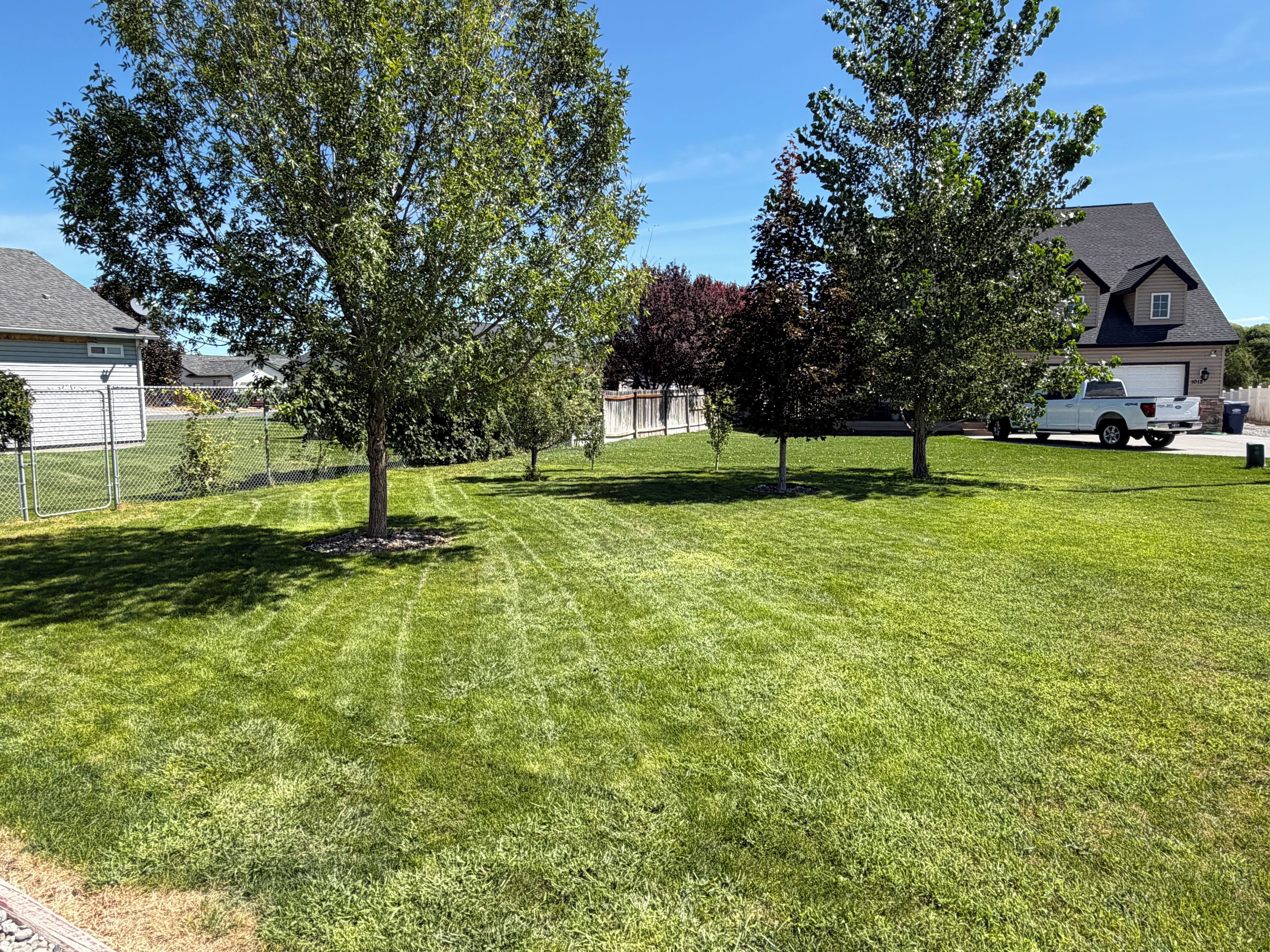 A well-maintained lawn with trees and a white pickup truck parked in the driveway.