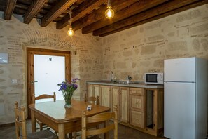 Eine rustikale Küche mit Steinwänden, Holzbalken, einem Holztisch mit Stühlen, einem weißen Kühlschrank und einer Mikrowelle.
