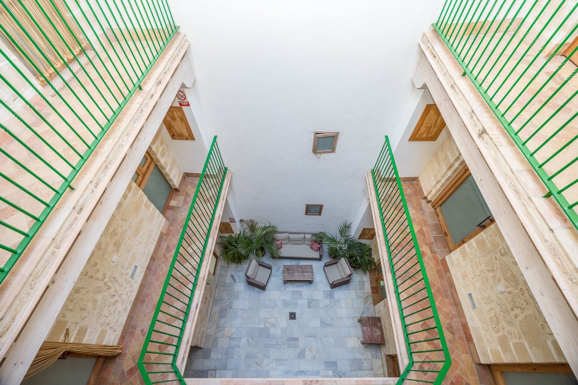Un edificio de varios niveles con una escalera central, barandillas de madera y piso de baldosas.
