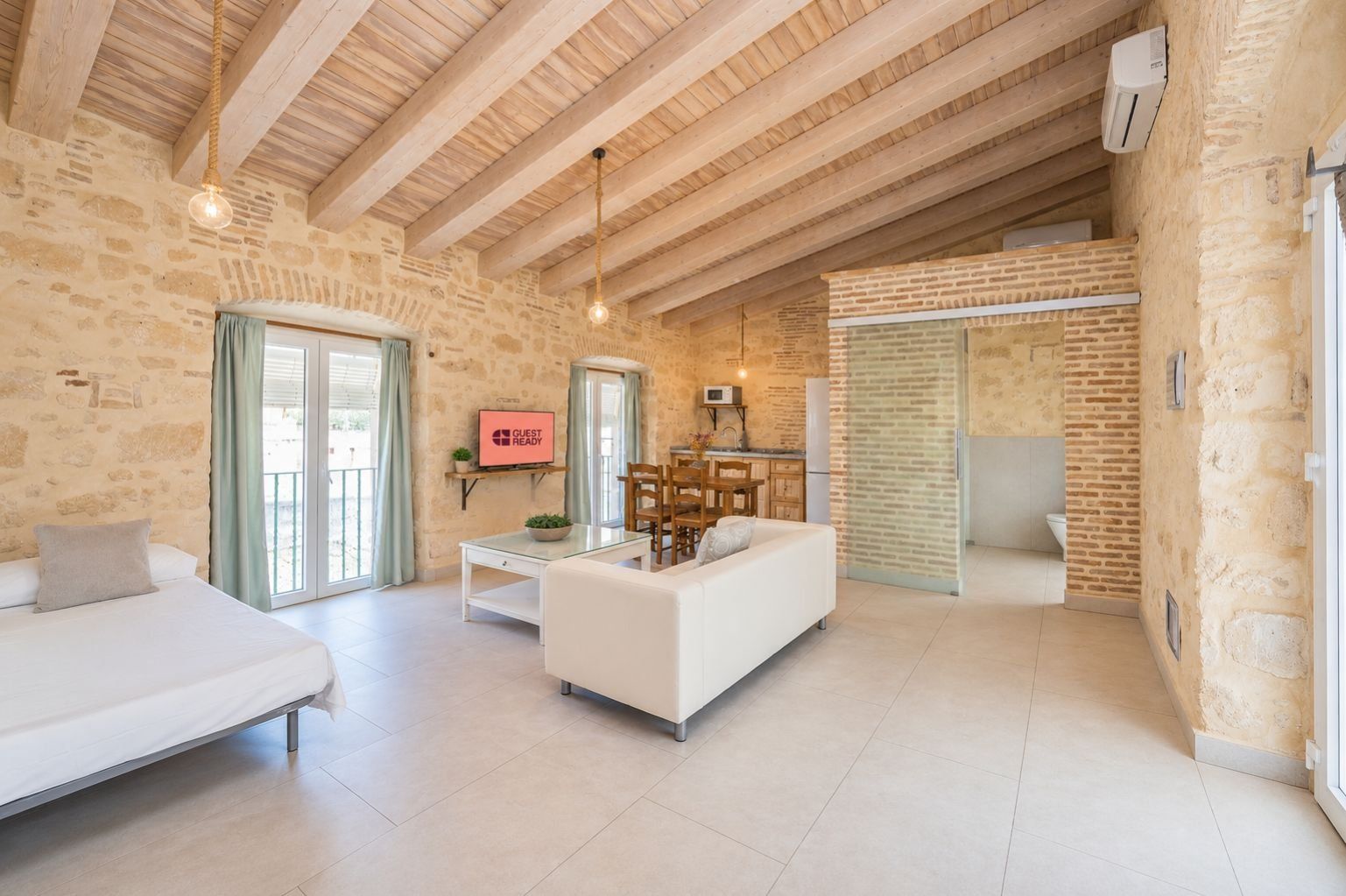 A spacious living area with a white sofa, a dining table, and a TV displaying 'GUEST READY'.