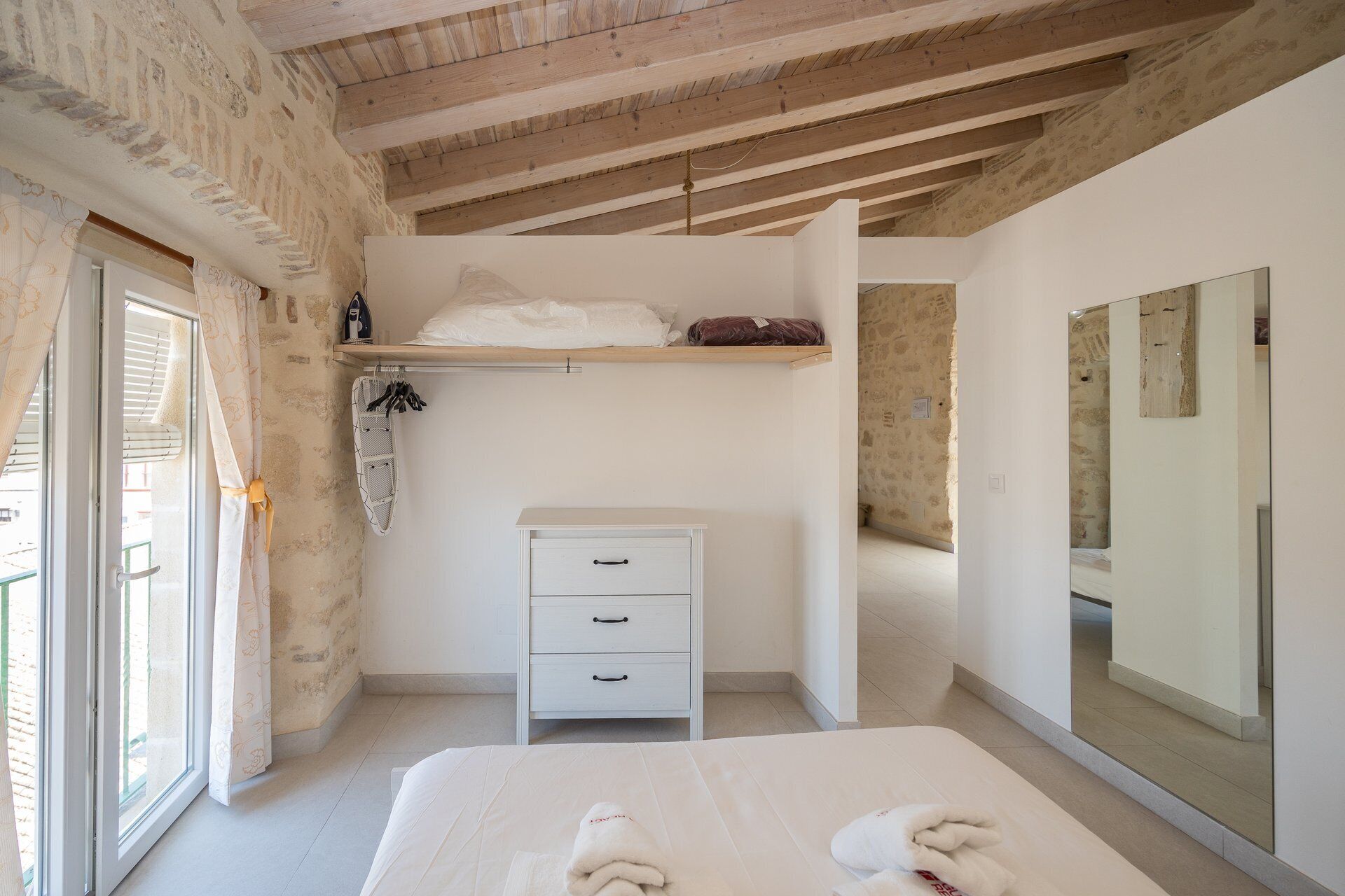 Un dormitorio con cama, cómoda, espejo y ventana con cortinas.