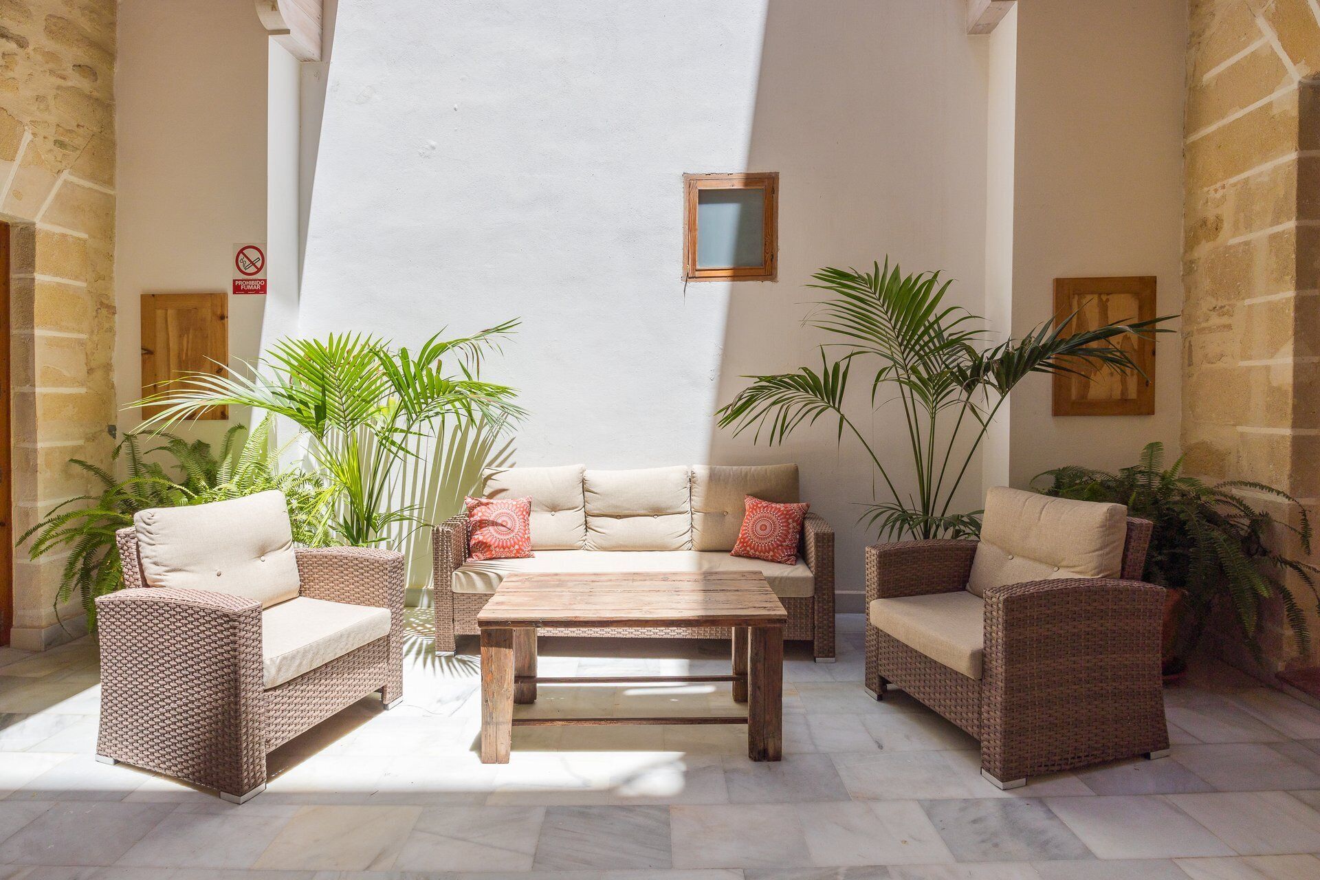 Un patio iluminado por el sol con muebles de mimbre, una mesa de madera y plantas en macetas.