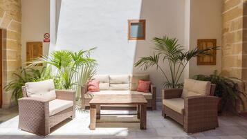 Un patio iluminado por el sol con muebles de mimbre, una mesa de madera y plantas en macetas.