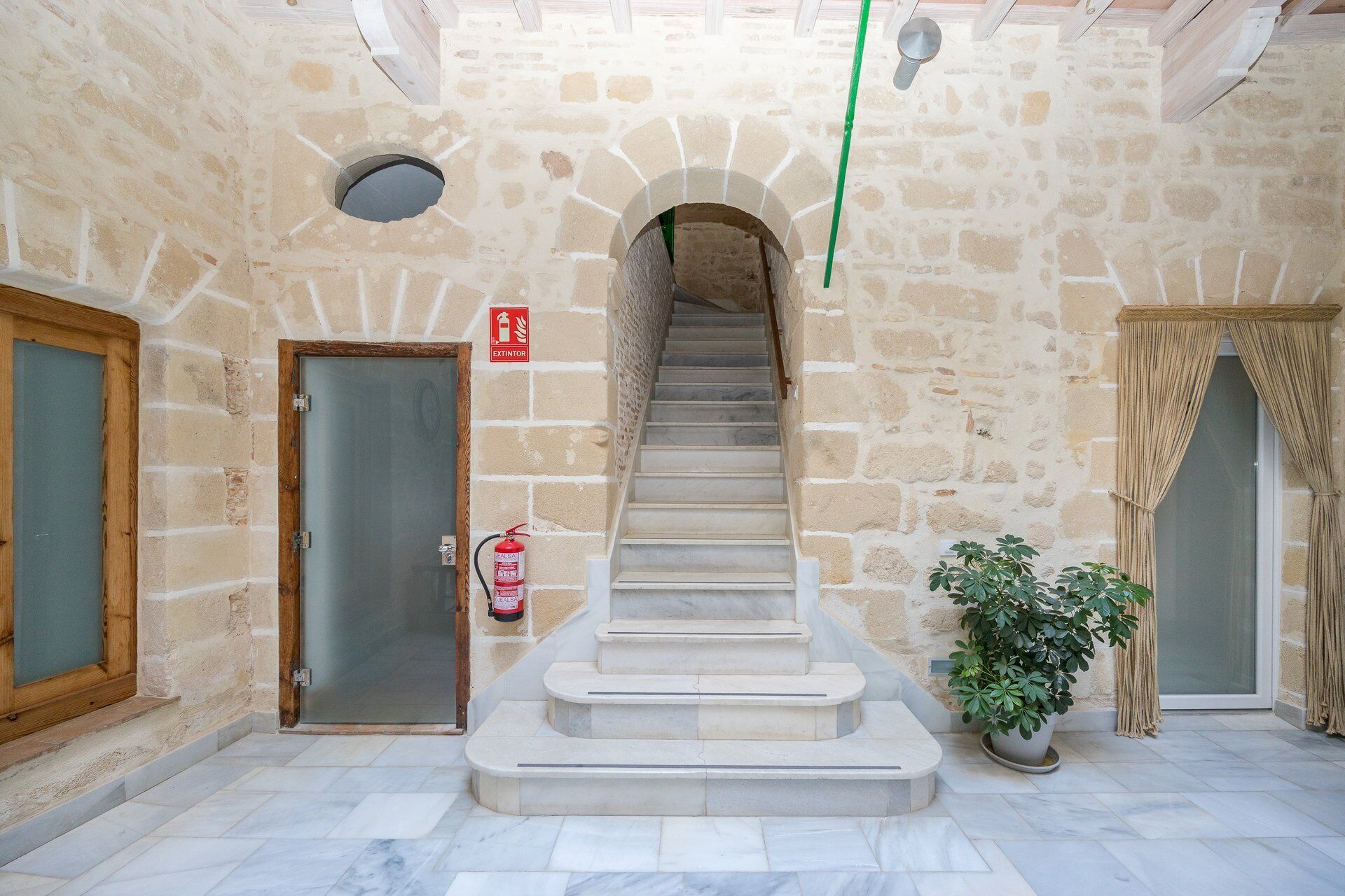 Una scala in pietra conduce a un piano superiore, con un estintore fissato al muro e una pianta in vaso vicino al fondo delle scale.