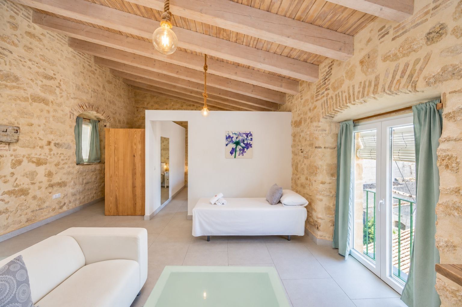 Una habitación con cama, sofá, una mesa de vidrio y vistas a través de una ventana.