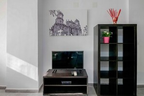 Ein Zimmer mit Flachbildfernseher auf einem Schrank, einem schwarzen Unterschrank mit Pflanze und einem an der Wand hängenden Kunstwerk.
