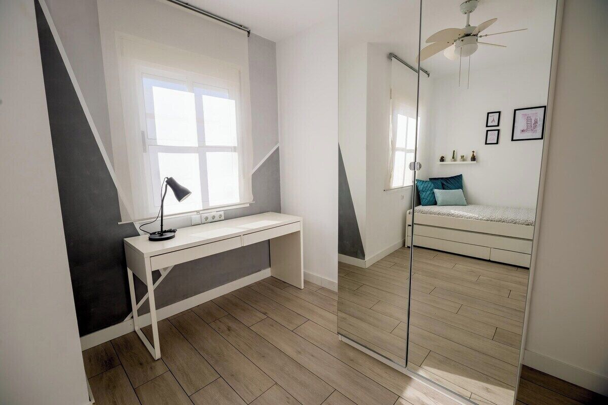 Un dormitorio con cama, escritorio, espejo y ventilador de techo.