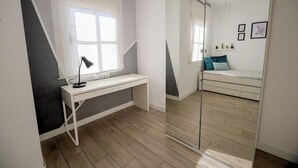 Ett sovrum med en säng, ett skrivbord, en spegel och en takfläkt.