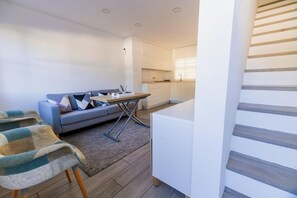 A modern living room with a sofa, a dining table, and a kitchen area in the background. - GuestReady - La Ostra (Chiclana de la Frontera)