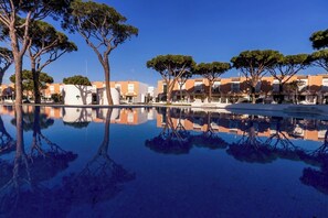 Ein Pool, der Bäume und Gebäude spiegelt, bei blauem Himmel.