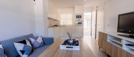 Un espace de vie moderne comprenant un canapé, une table basse, un téléviseur et une kitchenette.