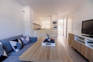 A modern living space with a sofa, coffee table, TV, and kitchenette. - GuestReady - La Ostra (Chiclana de la Frontera)