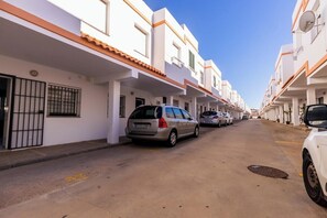 Eine Wohnstraße mit weißen Gebäuden, geparkten Autos und blauem Himmel.
