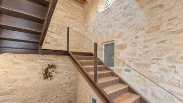 A staircase with wooden steps and glass railings, leading to a stone wall with a decorative wreath.