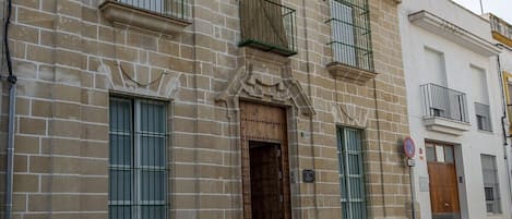 Um edifício com fachada tradicional, apresentando uma entrada central com porta de madeira, várias janelas com grades de metal e uma pequena varanda no andar superior.