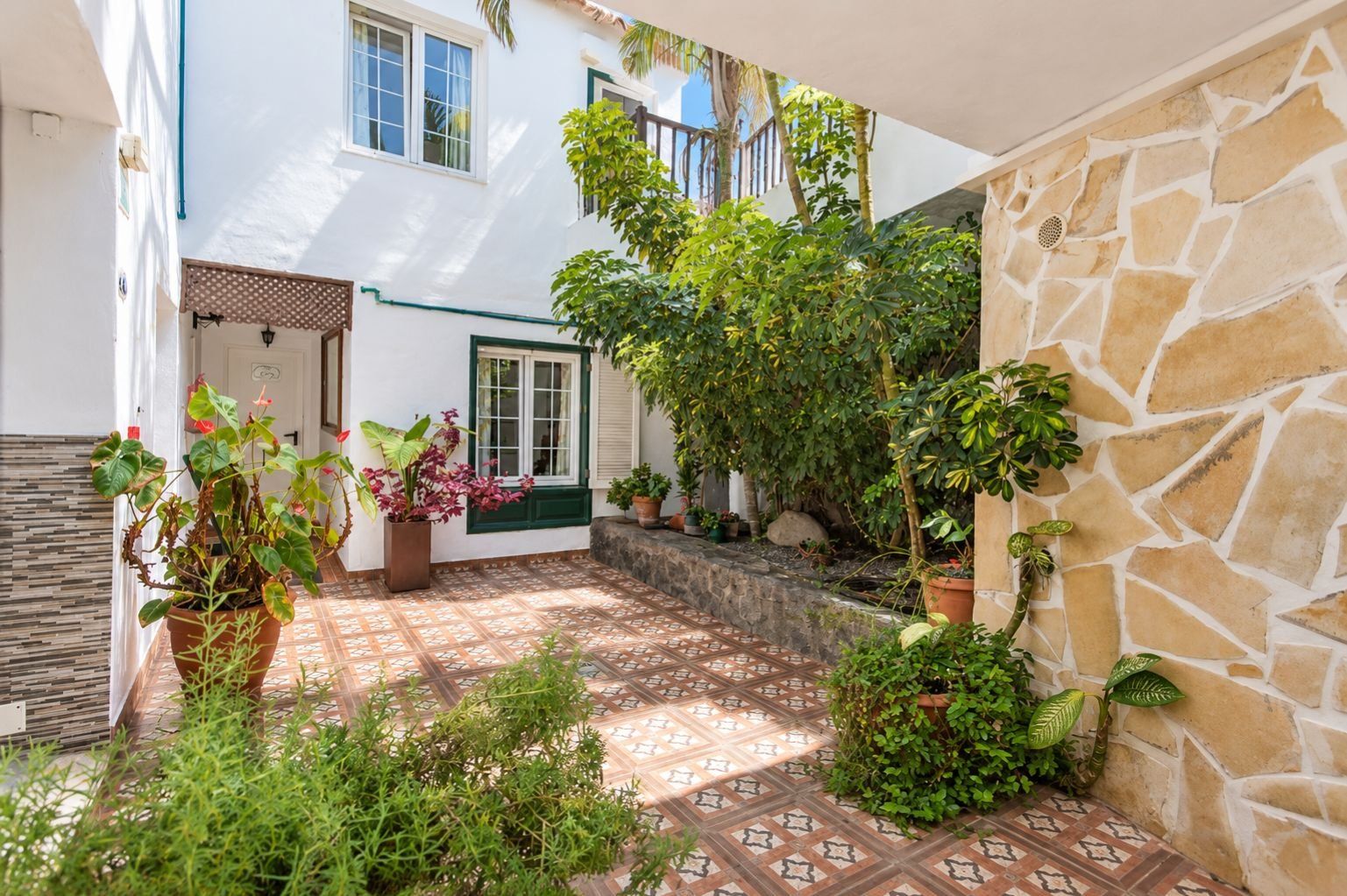 Un patio con suelo de baldosas, plantas en macetas y una pared de piedra.