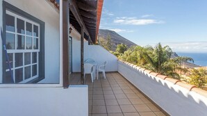 Ein Balkon mit Blick auf das Meer und die Berge, weiße Wände und ein gefliester Boden.