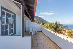 Ein Balkon mit Blick auf das Meer und die Berge, weiße Wände und ein gefliester Boden.