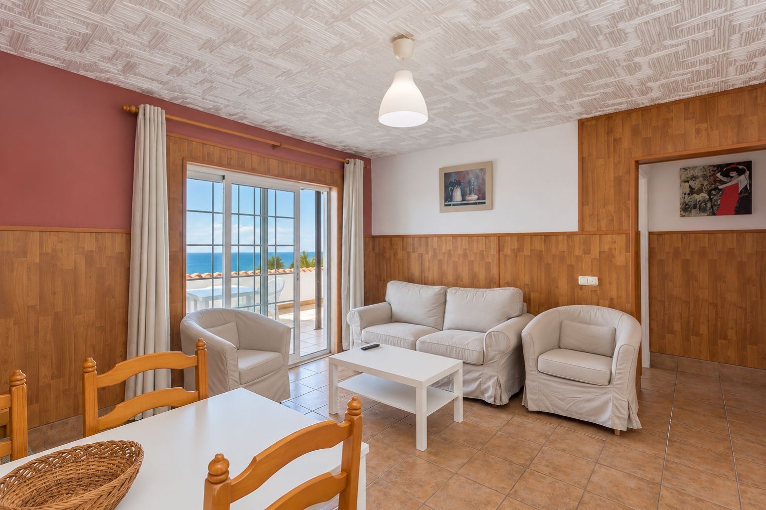 Ein Zimmer mit Holzboden, einem weißen Tisch, zwei Sofas und Meerblick durch eine Glastür.