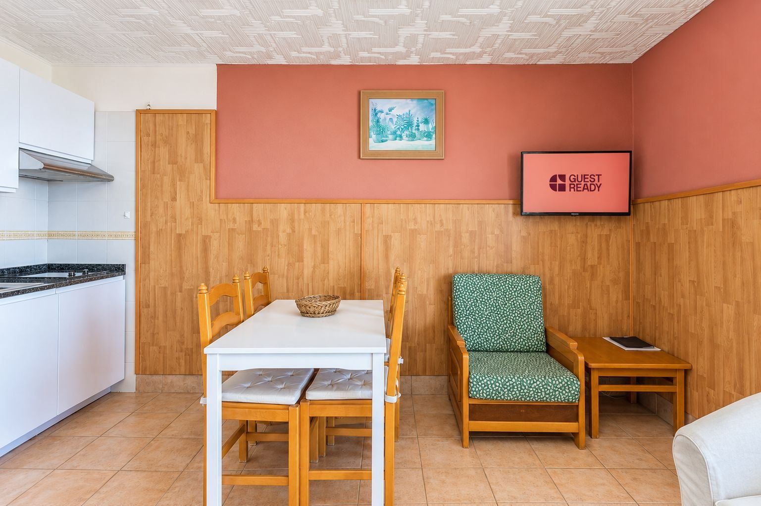 Une pièce de taille modeste comprenant une table à manger, une chaise, une petite table de chevet et un téléviseur affichant le message « CHAMBRE PRÊTE POUR L’ARRIVÉE DES CLIENTS ».
