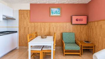 Une pièce de taille modeste comprenant une table à manger, une chaise, une petite table de chevet et un téléviseur affichant le message « CHAMBRE PRÊTE POUR L’ARRIVÉE DES CLIENTS ».