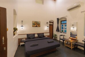 A bedroom with a large bed, bedside lamps, a painting, a window with curtains, and an air conditioning unit.