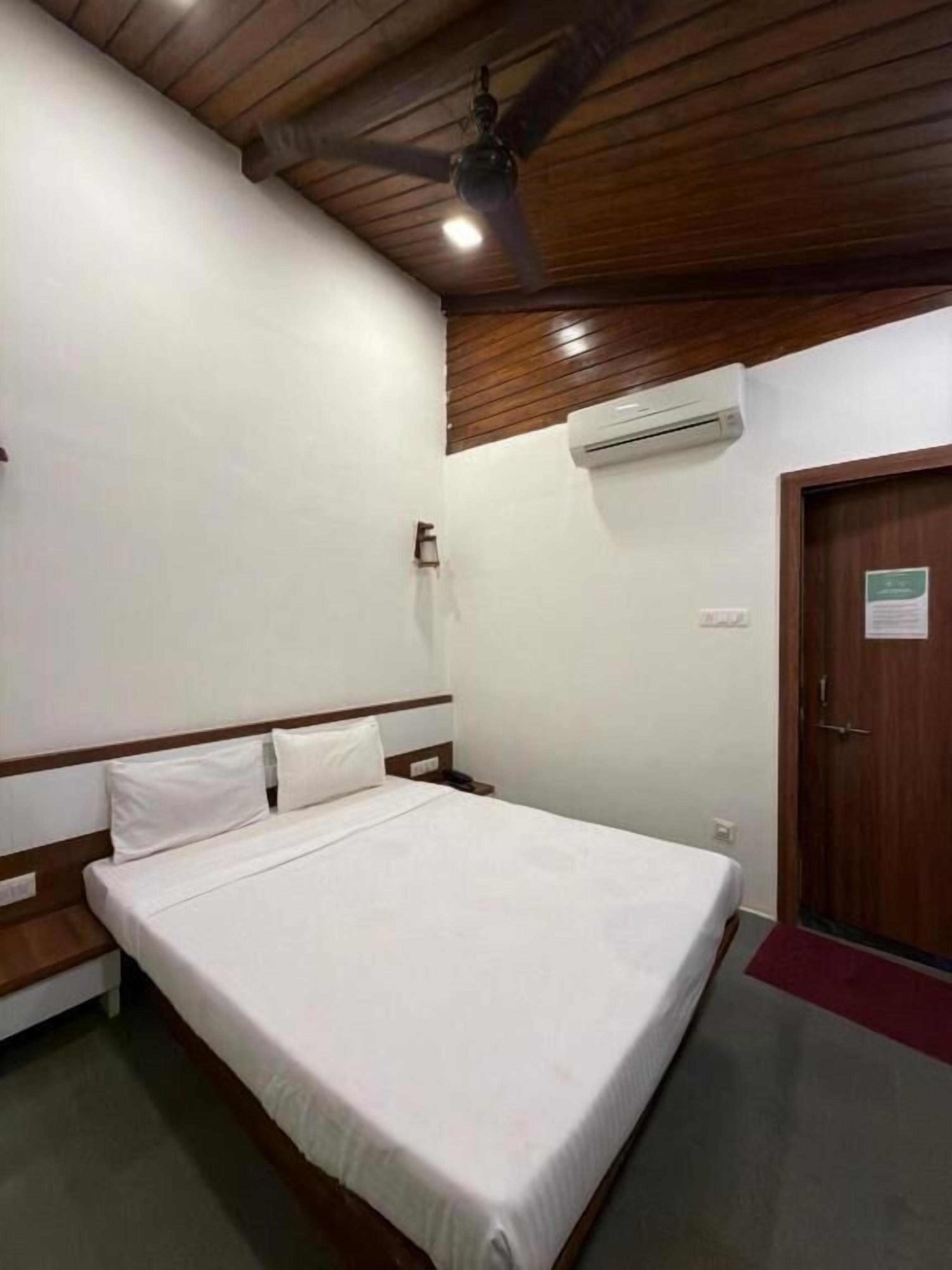 Habitación individual con una cama y cabecera de madera, un equipo de aire acondicionado en la pared y una puerta con un letrero.