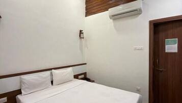 Habitación individual con una cama y cabecera de madera, un equipo de aire acondicionado en la pared y una puerta con un letrero.
