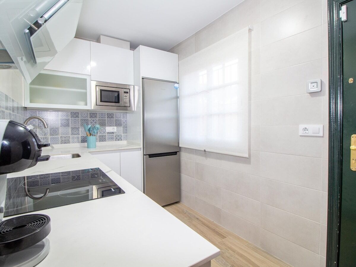 Een moderne keuken met witte kasten, een roestvrijstalen koelkast, een magnetron en een waterkoker.