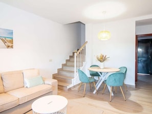 A living room with a sofa, a round table with chairs, a staircase, and a door. - GuestReady - Chiclana Labarrosa (Chiclana de la Frontera)