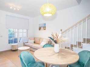 Un salon moderne avec une table ronde en bois, des fauteuils turquoise, un canapé beige et un escalier avec des rampes blanches.