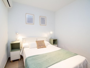 A hotel room with a bed, nightstands, a green blanket, and two framed pictures on the wall. - GuestReady - Chiclana Labarrosa (Chiclana de la Frontera)