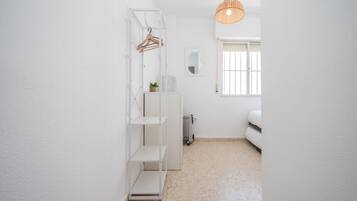 Een kleine kamer met witte wanden, een bed, een radiator, een hanglamp en een raam met blinds.