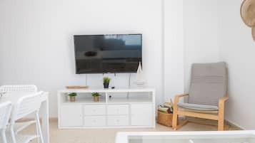 En stue med et fladskærms-tv på væggen, et hvidt tv-møbel med opbevaring, en grå polstret stol og et hvidt sofabord.