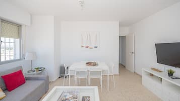 En moderne stue med en hvid sofa, et spisebord med stole, et fjernsyn på et stativ og et maleri på væggen.