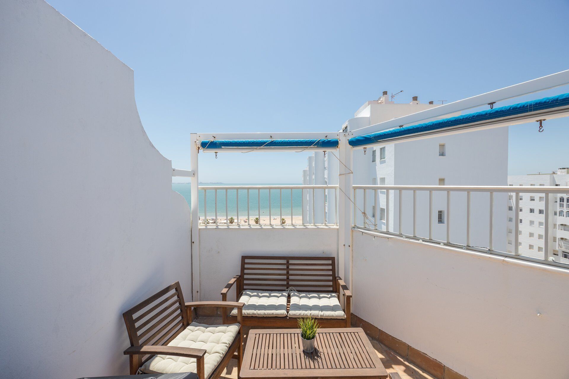 Un balcón con vista a la playa, muebles de madera y una planta en maceta.