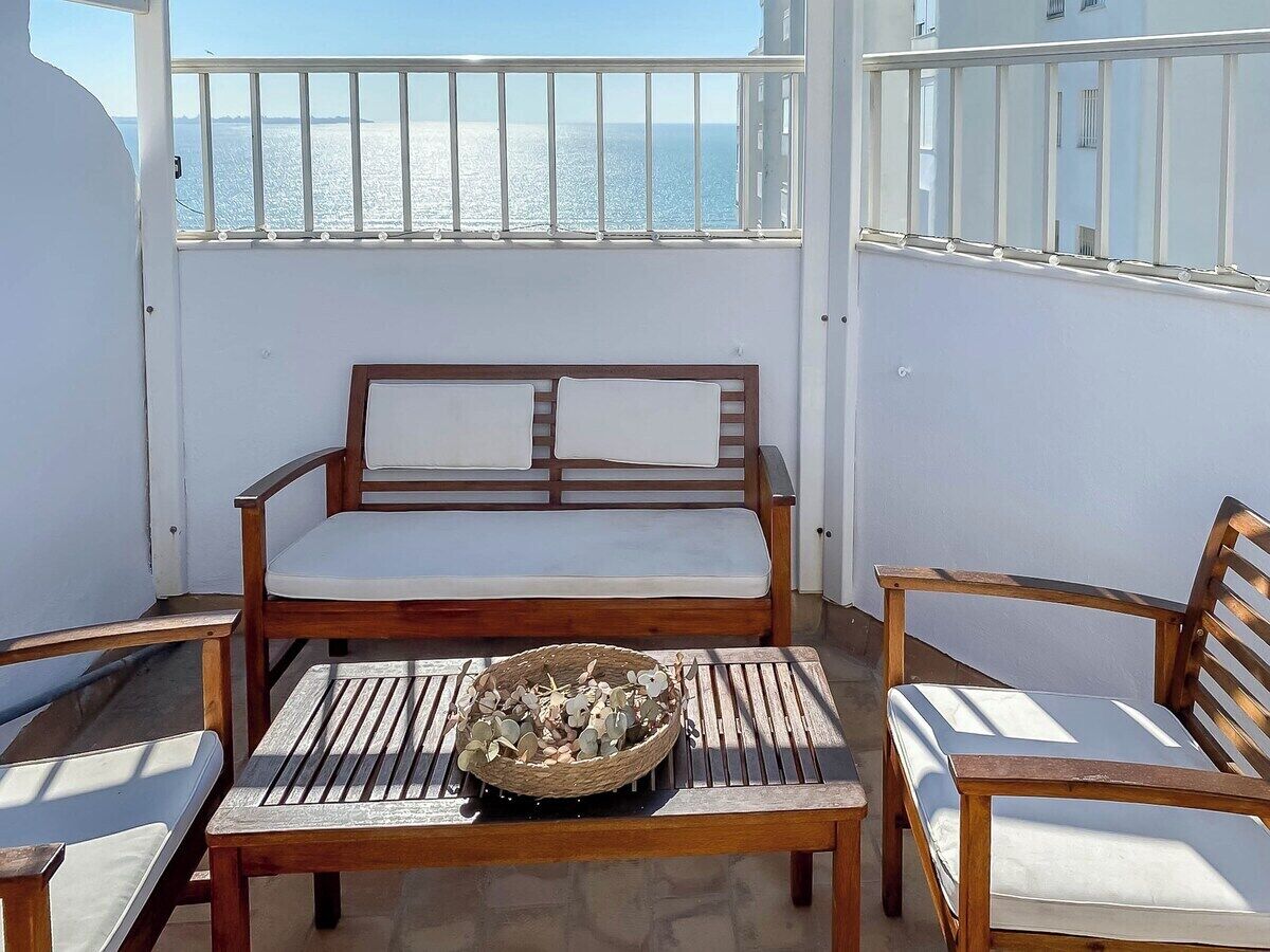 A balcony with a wooden sofa, two wooden chairs, a small table, and a basket of decorative items.