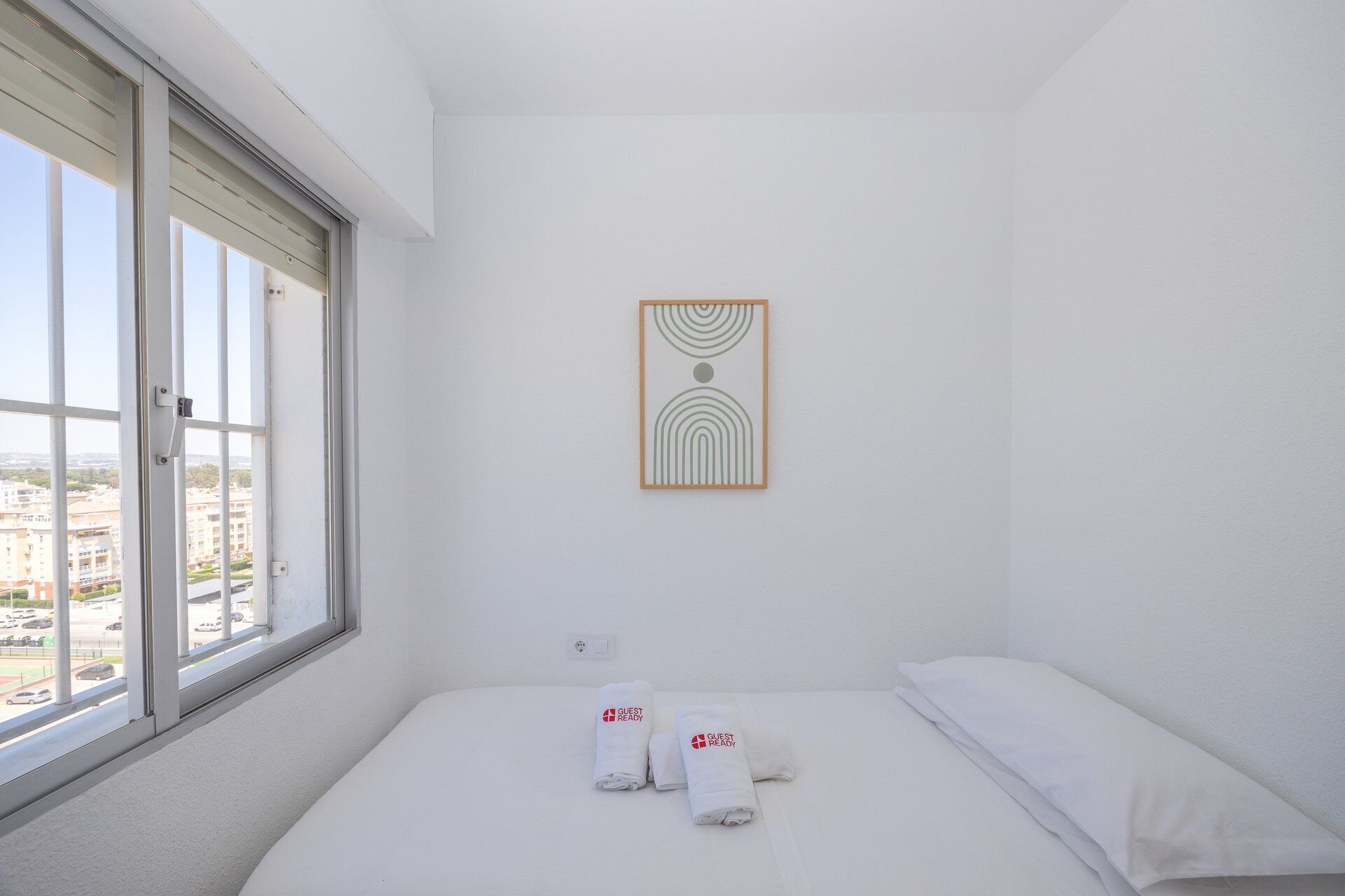 A hotel room with a bed, a window, and a wall-mounted artwork.