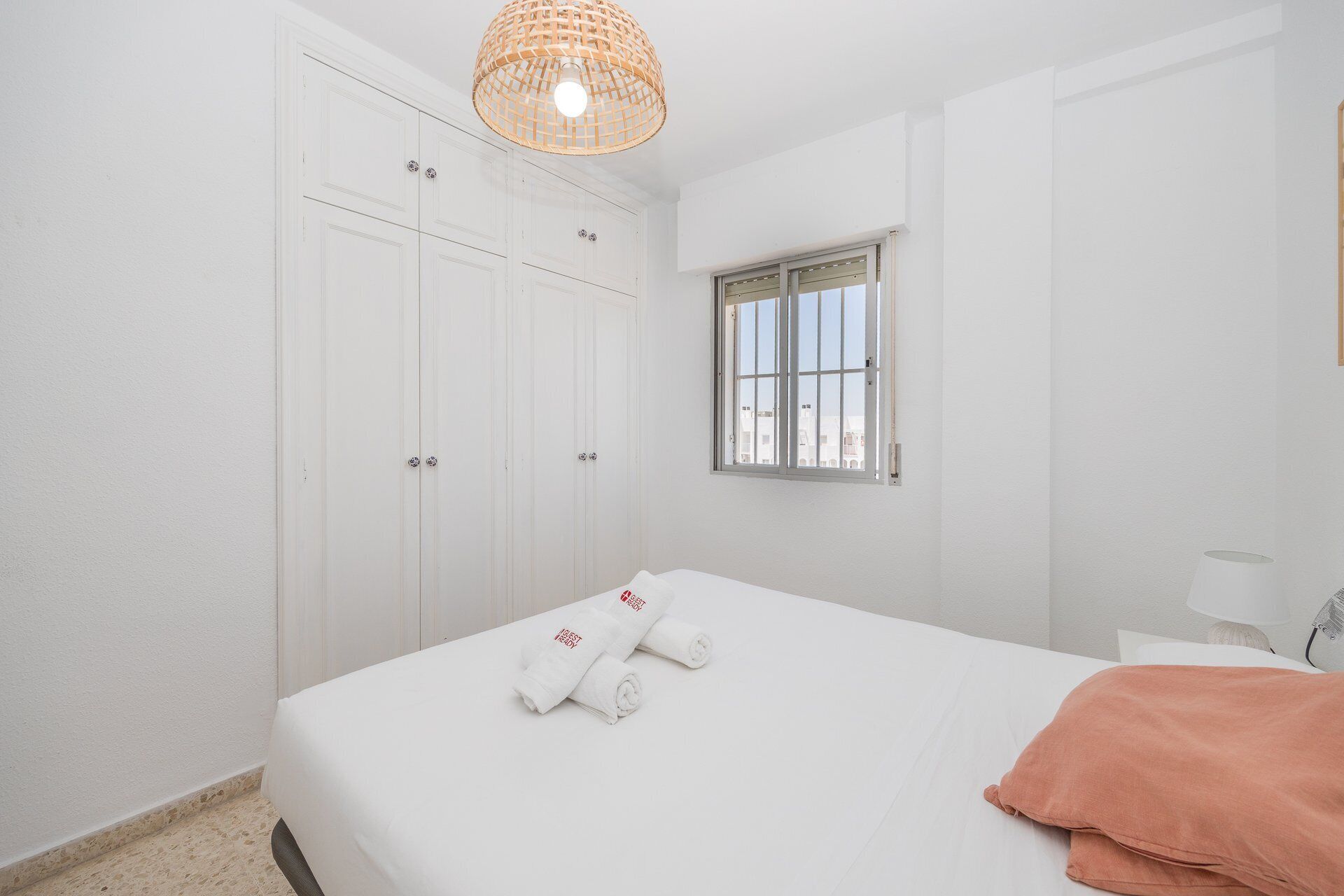 Habitación de hotel con cama, ventana con barrotes, armario y lámpara colgante.