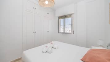 Habitación de hotel con cama, ventana con barrotes, armario y lámpara colgante.