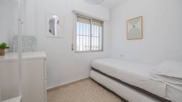 Ein Schlafzimmer mit einem Bett, einem Fenster, einem an der Wand befestigten Spiegel und einer kleinen Pflanze auf einem Regal.