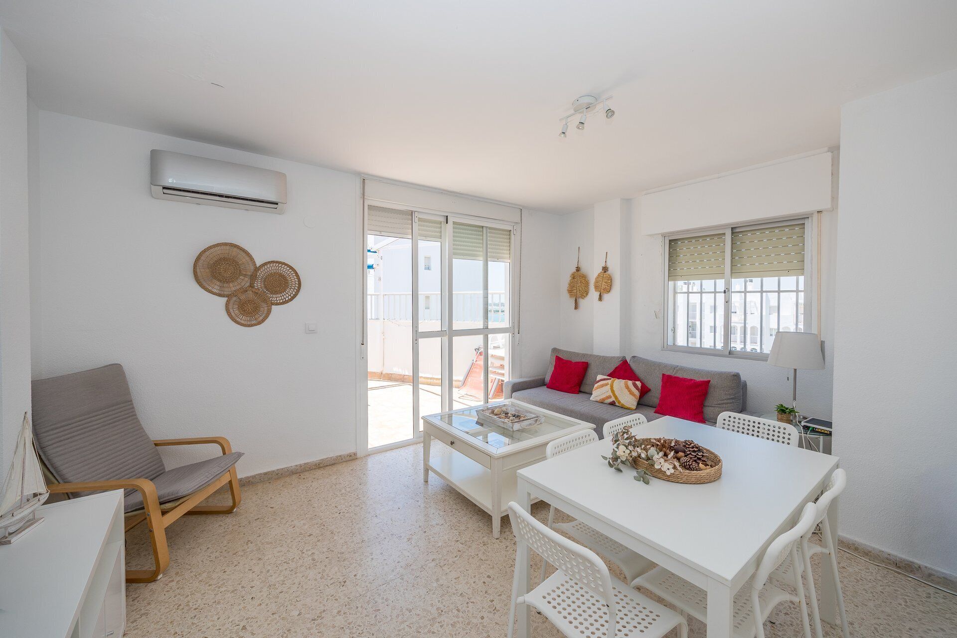 Ein modernes Wohnzimmer mit einer Couch, einem Esstisch und einem Sessel. Es gibt ein Fenster mit Jalousien, einen Deckenventilator und eine Klimaanlage.