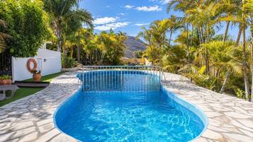 Una piscina con borde de azulejos, rodeada de palmeras y una montaña al fondo.