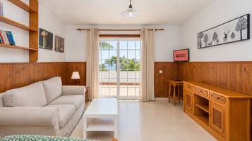 A furnished living room with a sofa, a small table, a cabinet, and a view through a glass door.