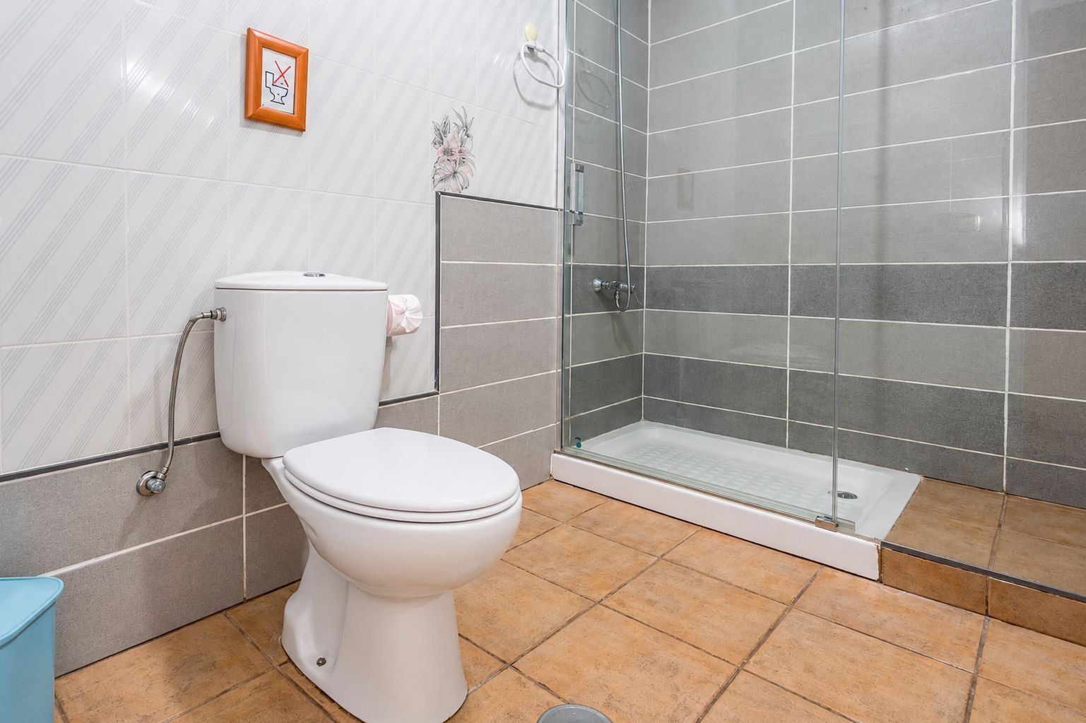 Un baño con inodoro, cabina de ducha de vidrio y piso de baldosas.